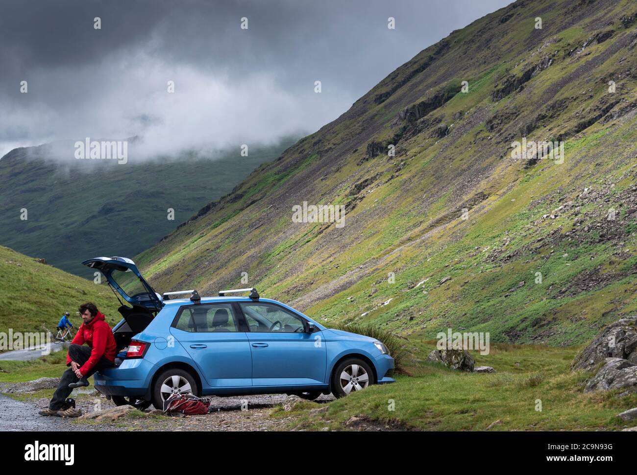 Escursionista nel Lake District tornando alla sua auto dopo una passeggiata nel Parco Nazionale. Wrynose Pass, Cumbria, Regno Unito. Foto Stock