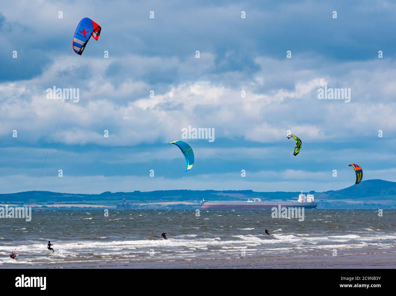 I kite surfisti kite surfing in giornata ventosa con la petroliera ancorata all'orizzonte a Firth of Forth, Scozia, Regno Unito Foto Stock