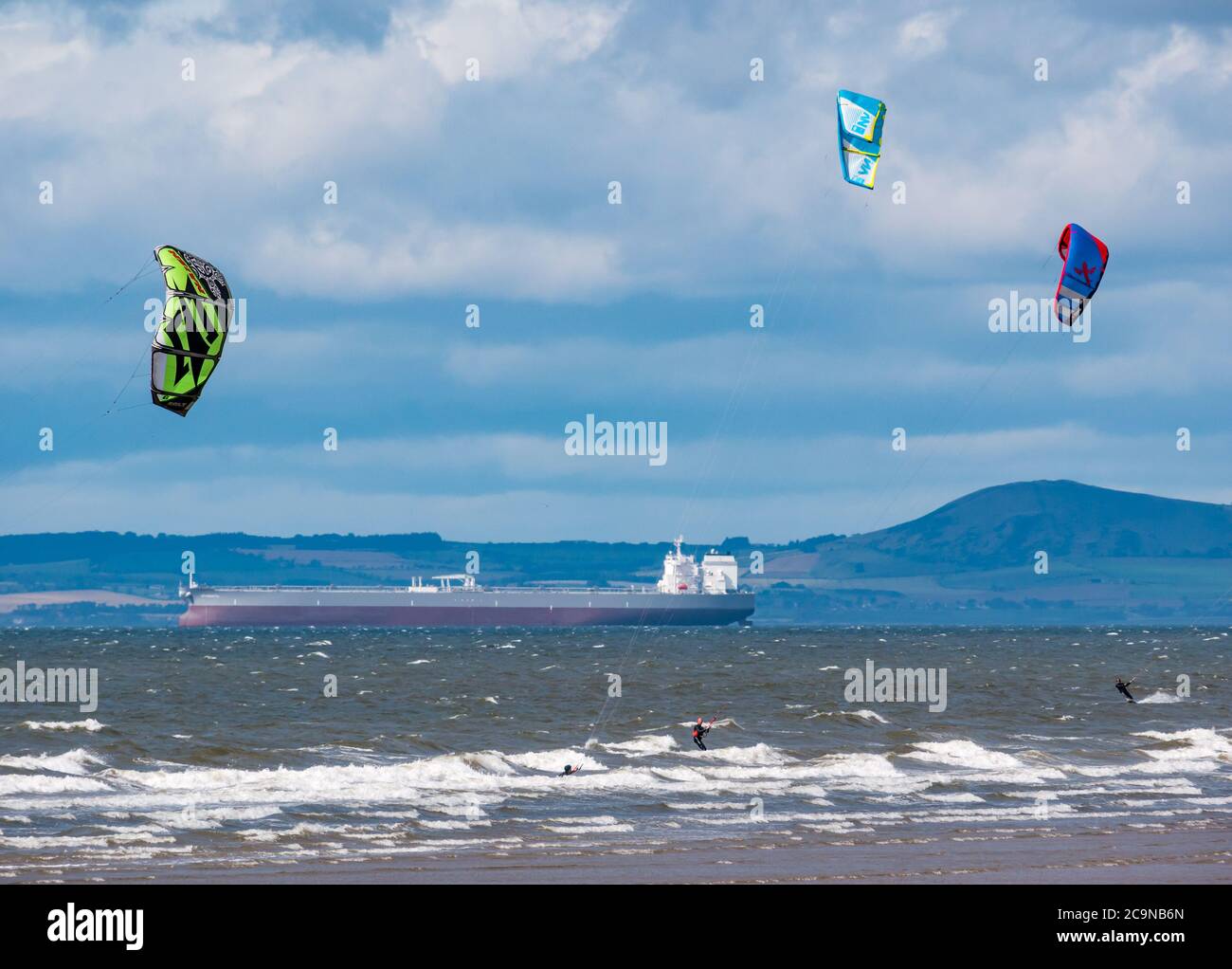 I kite surfisti kite surfing in giornata ventosa con la petroliera ancorata all'orizzonte a Firth of Forth, Scozia, Regno Unito Foto Stock