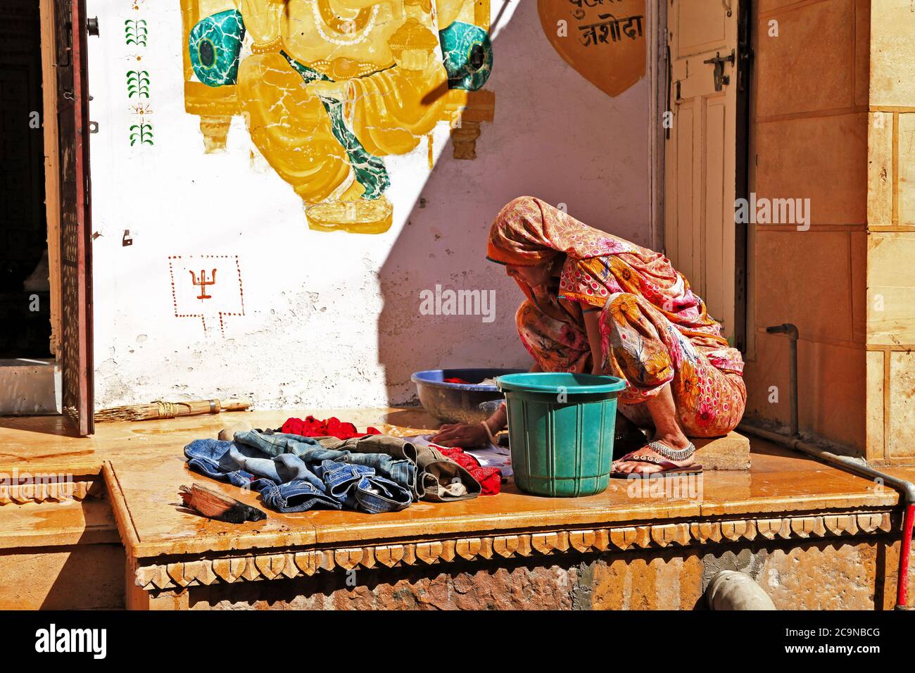India vita di giorno. Jaisalmer città vecchia 'strade, donna lavaggio abiti. 13 febbraio Rajastan, India Foto Stock