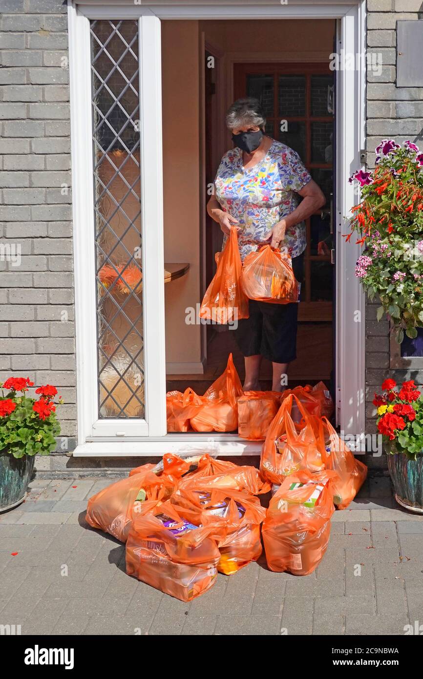 Senior pensionato in Covid 19 maschera viso sposta cibo alimentari Borse di plastica dopo Sainsburys consegna borsa e mantiene sicuro Distanza sociale Regno Unito Foto Stock