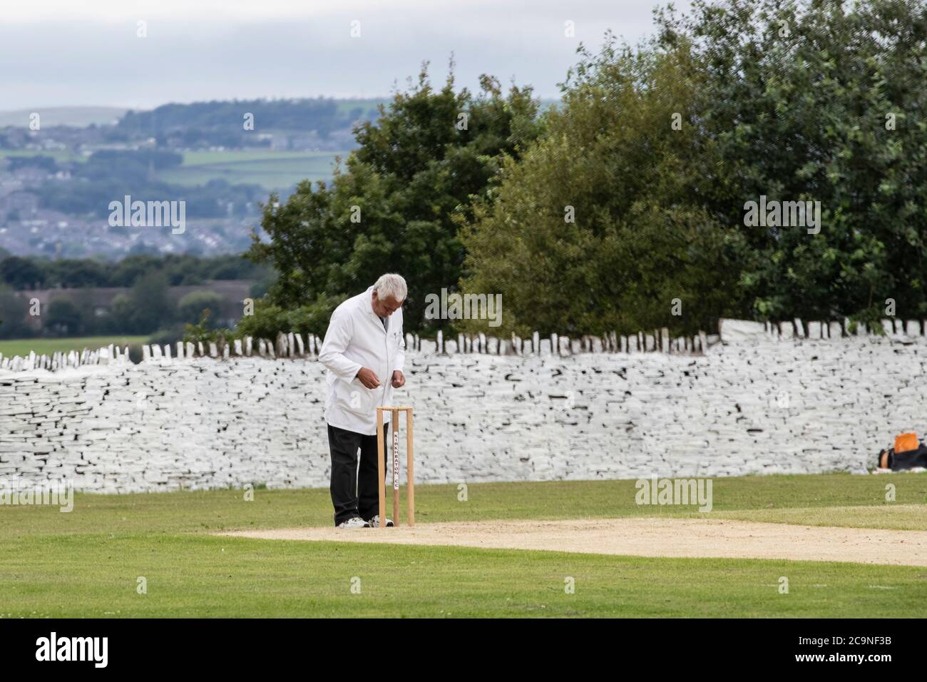 Cricket umpire dietro le parate consultando un notebook mentre officiando ad una partita di cricket villaggio in West Yorkshire in un Sabato pomeriggio Foto Stock