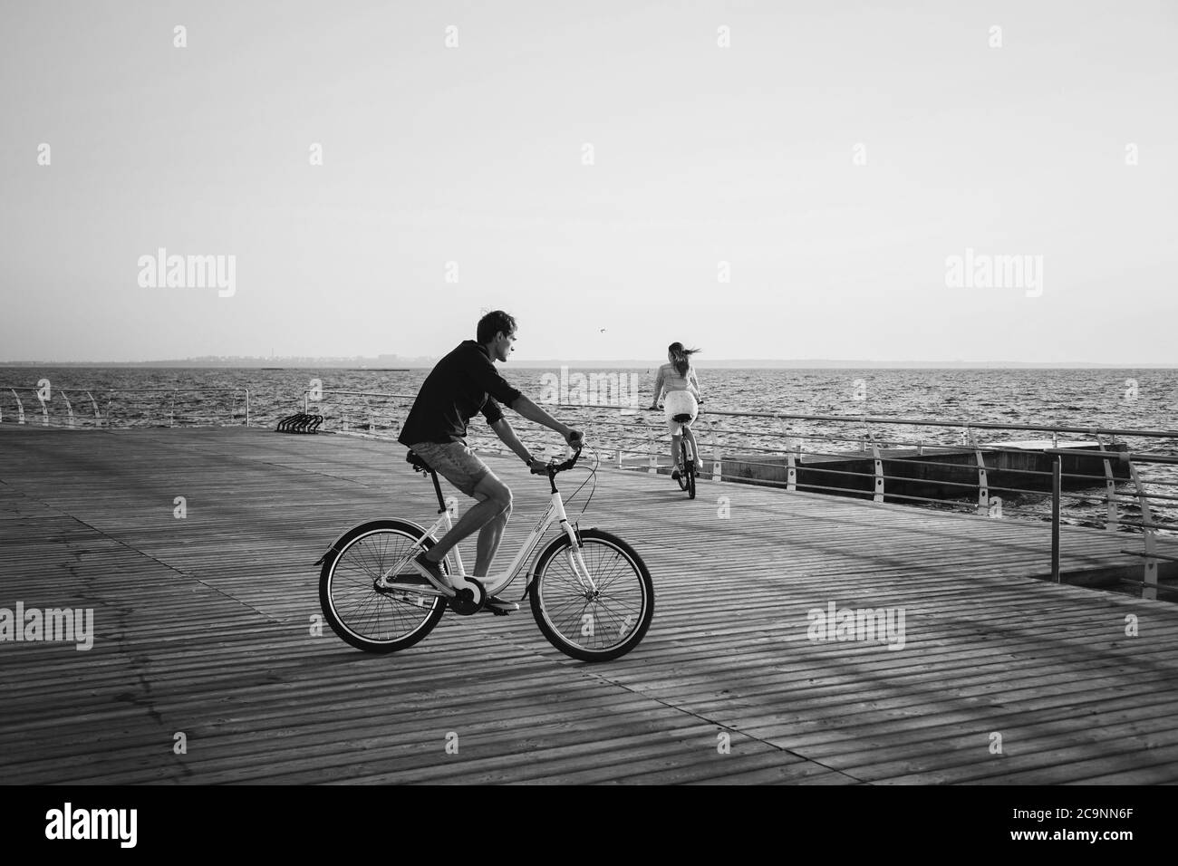 Coppia di giovani hipster che pedalano insieme sulla spiaggia al cielo dell'alba sul ponte di legno durante l'estate Foto Stock
