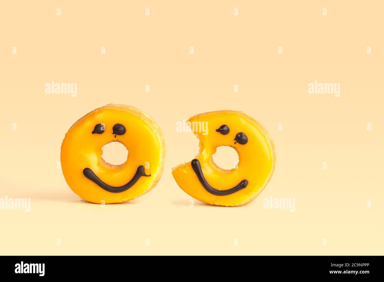 Due ciambelle gialle fresche con un sorriso al cioccolato, un morso mancante isolato su sfondo giallo con ombra morbida Foto Stock