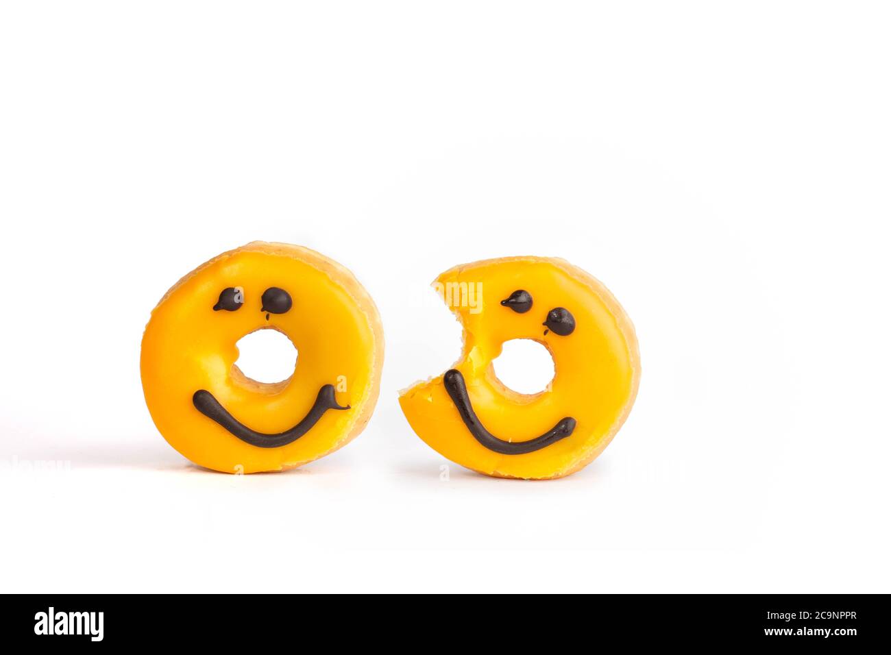 Due ciambelle gialle fresche con un sorriso al cioccolato, un boccone mancante isolato su sfondo bianco con ombra morbida Foto Stock