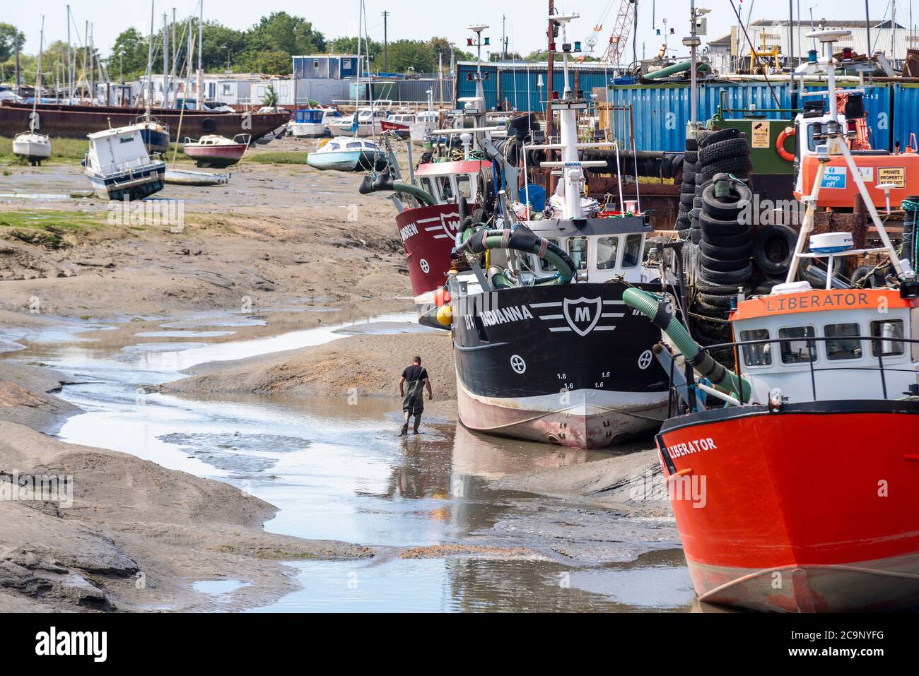 Flotta di pesca con bassa marea a Old Leigh, Leigh on Sea, Essex, Regno Unito. Persona in piedi da grande peschereccio per la scala. Barche da pesca, navi. Increspatura Foto Stock