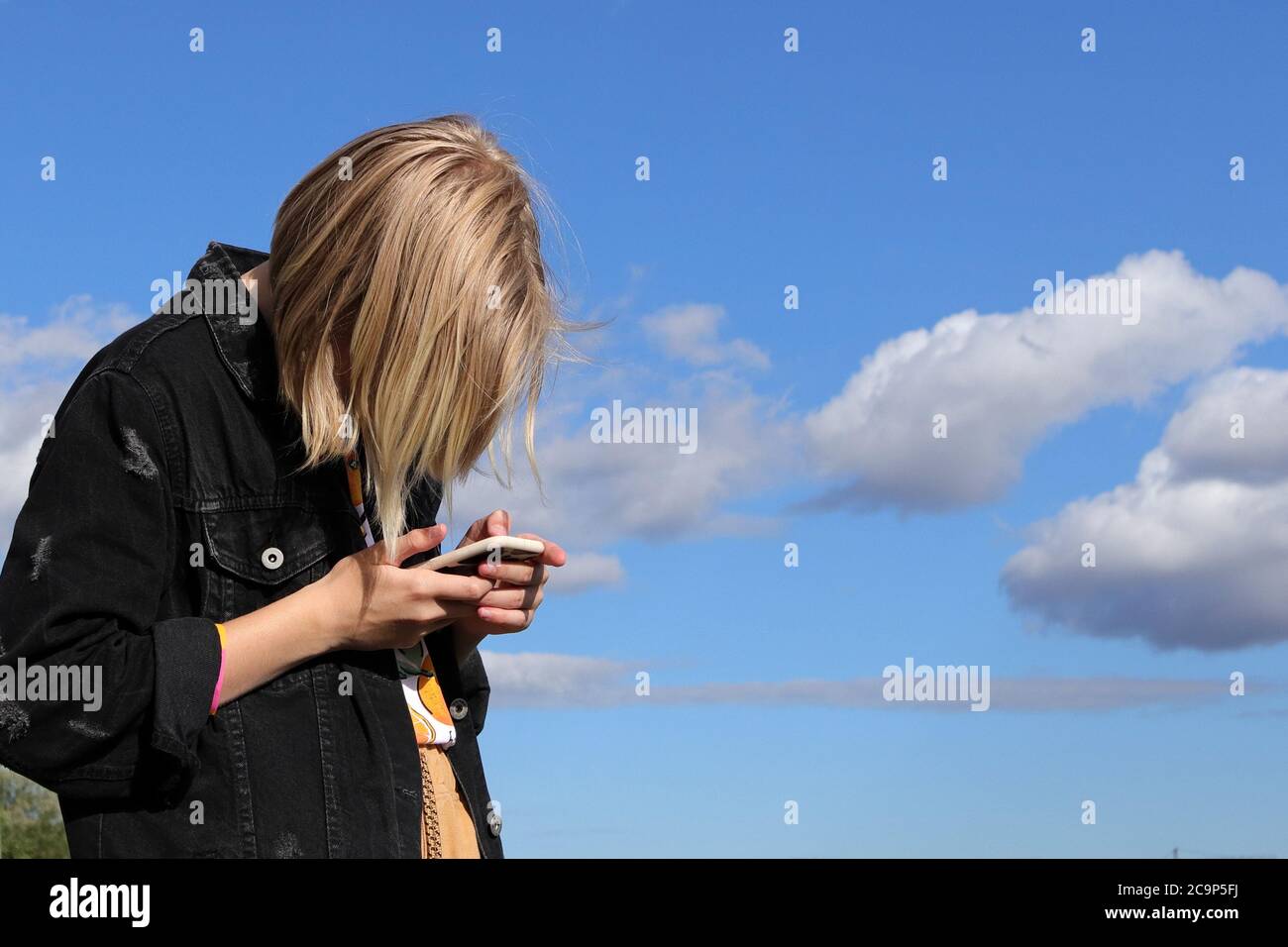 Ragazza teen che gioca online giochi da uno smartphone su sfondo cielo blu. Il concetto di dipendenza adolescente da un telefono cellulare e social network Foto Stock