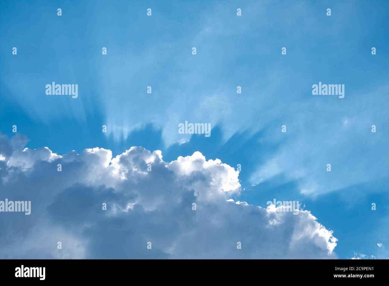 Sole dietro una nuvola bianca. Cielo estivo blu sullo sfondo. Corona di raggi solari. Foto Stock