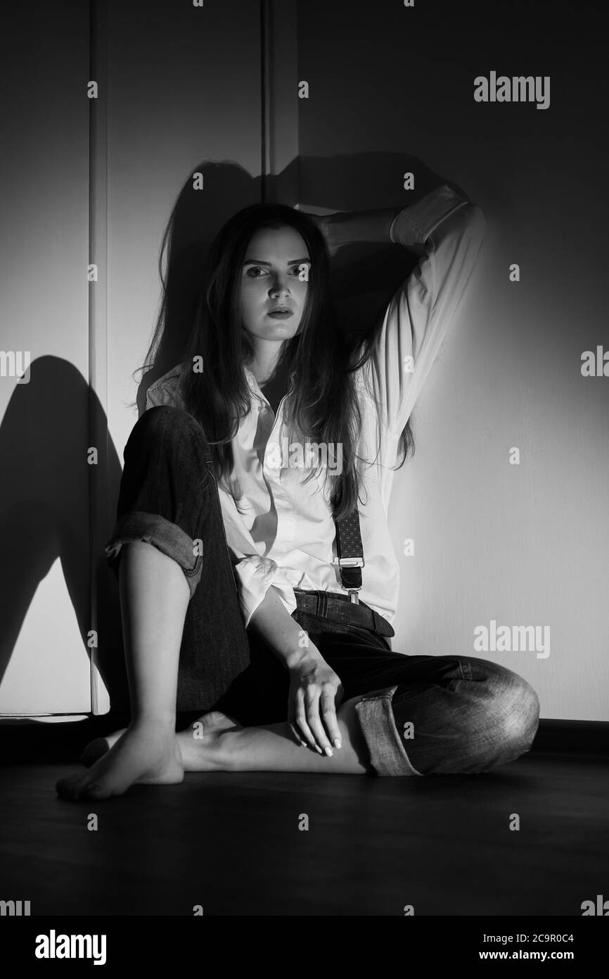 donna triste seduta in angolo sul pavimento in camera oscura, monocromatica Foto Stock