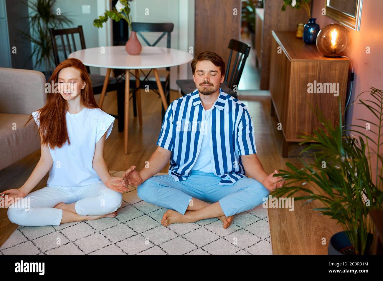 ragazza rossa e ragazzo bearded coinvolti nello yoga, giovane coppia sposata condurre uno stile di vita sano, pratica yoga, in posa di loto Foto Stock