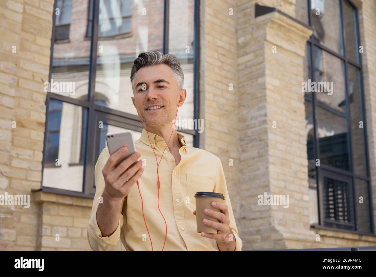 Bell'uomo che tiene il telefono cellulare, bere caffè, guardare lo schermo digitale, leggere notizie. Uomo d'affari sorridente utilizzando il cellulare, lo shopping online Foto Stock