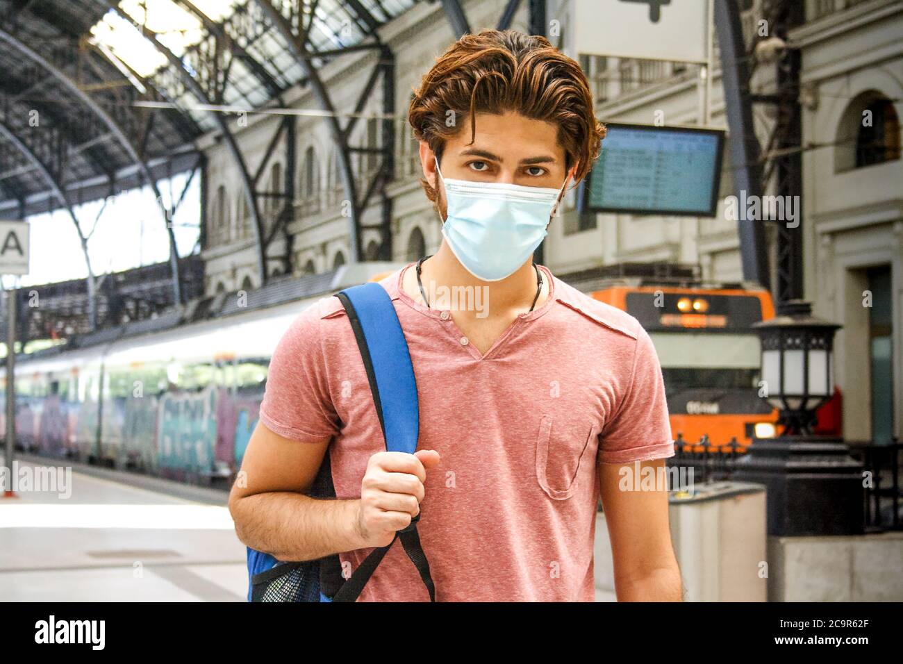 Giovane uomo che lascia la stazione ferroviaria con maschera facciale attivata. Scatto medio. Foto Stock