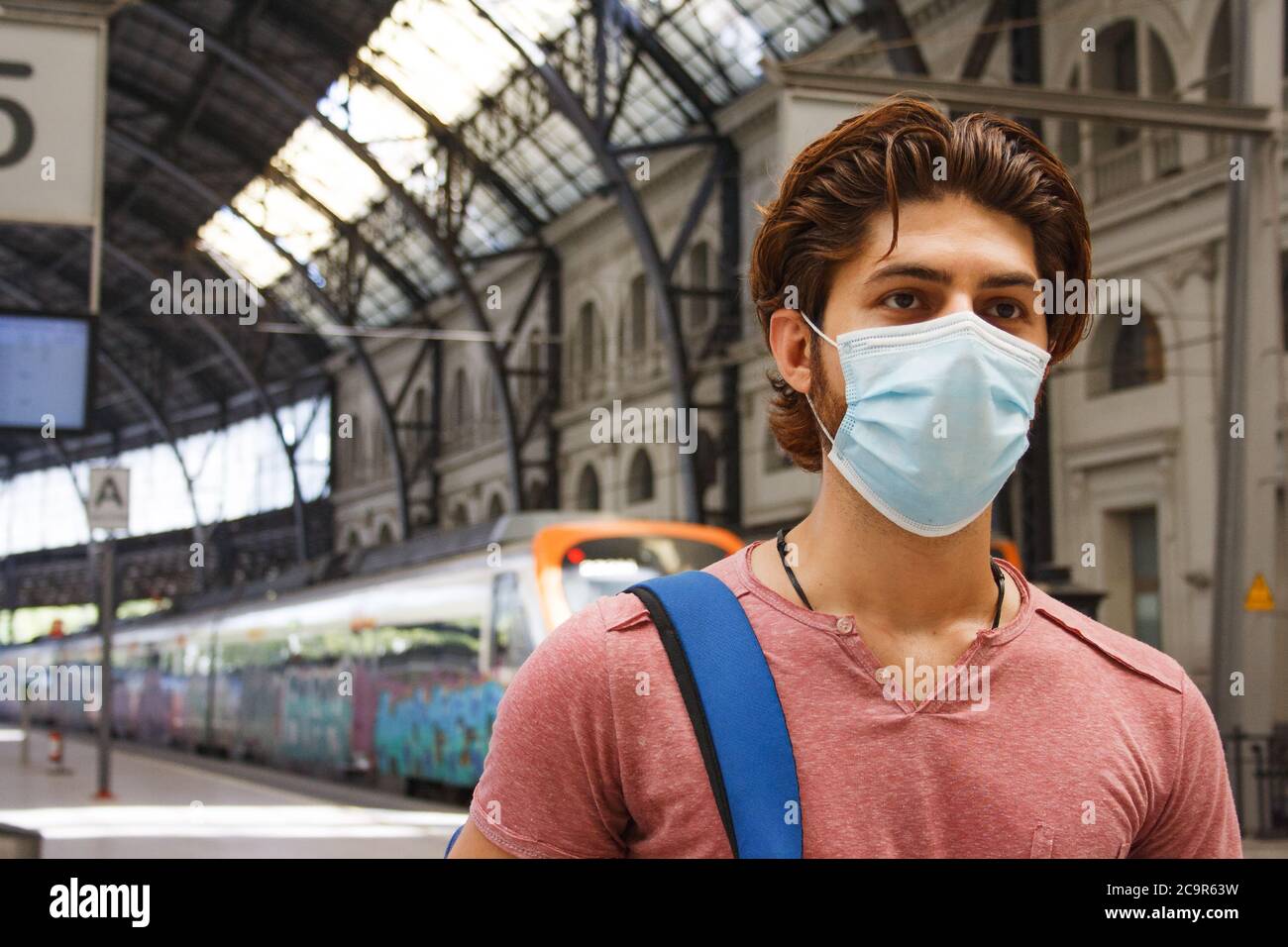 Giovane uomo che lascia la stazione ferroviaria con maschera facciale attivata. Primo piano. Foto Stock