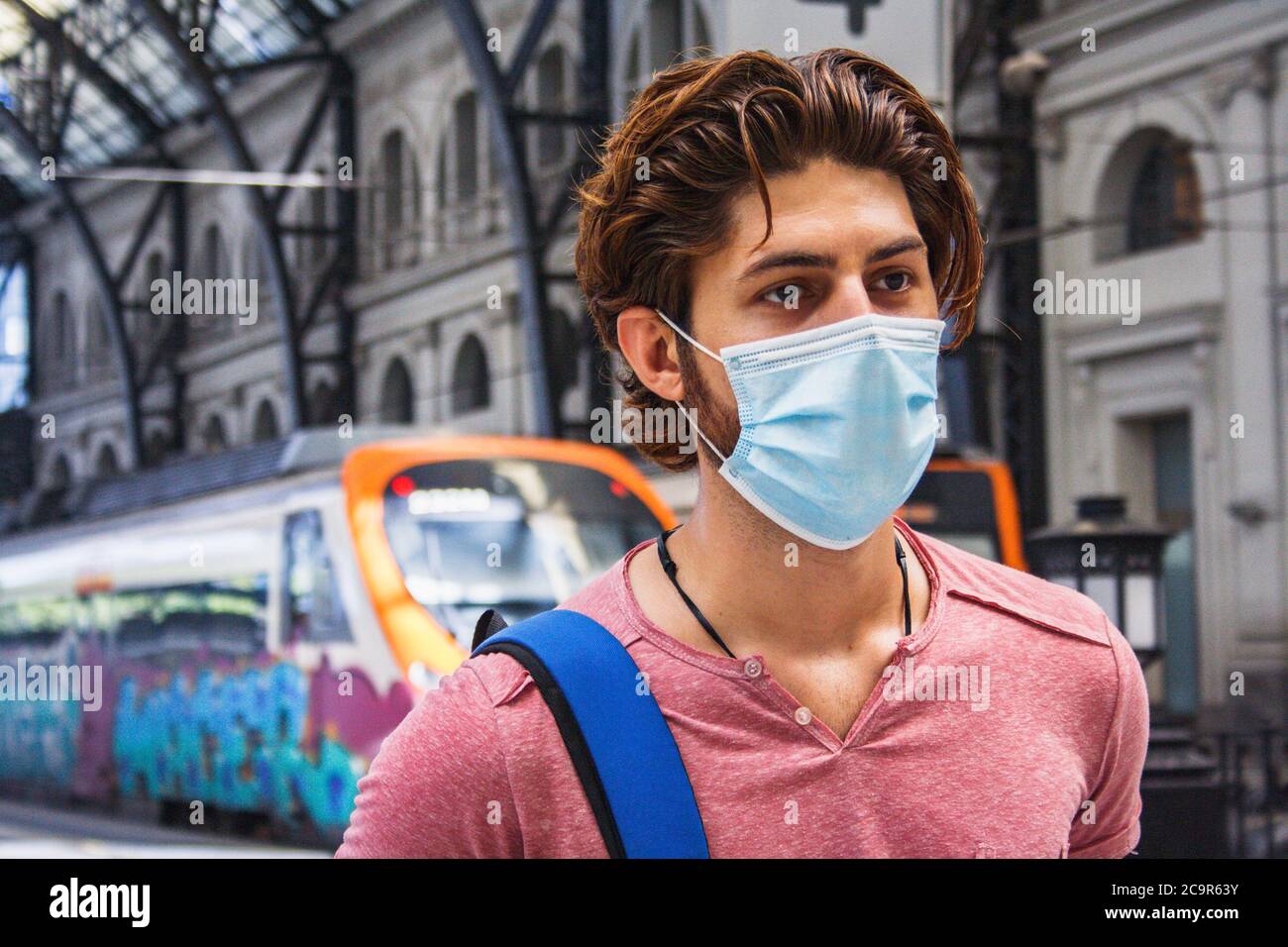 Giovane uomo che lascia la stazione ferroviaria con maschera facciale attivata. Primo piano. Foto Stock