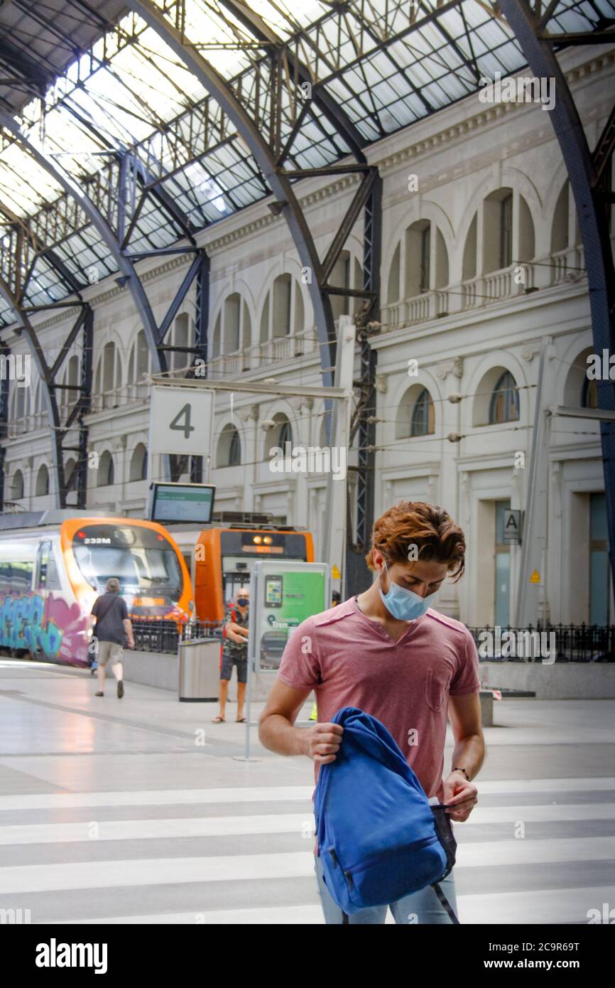 Giovane uomo che lascia la stazione ferroviaria con maschera facciale attivata. Zaino carring. Foto Stock