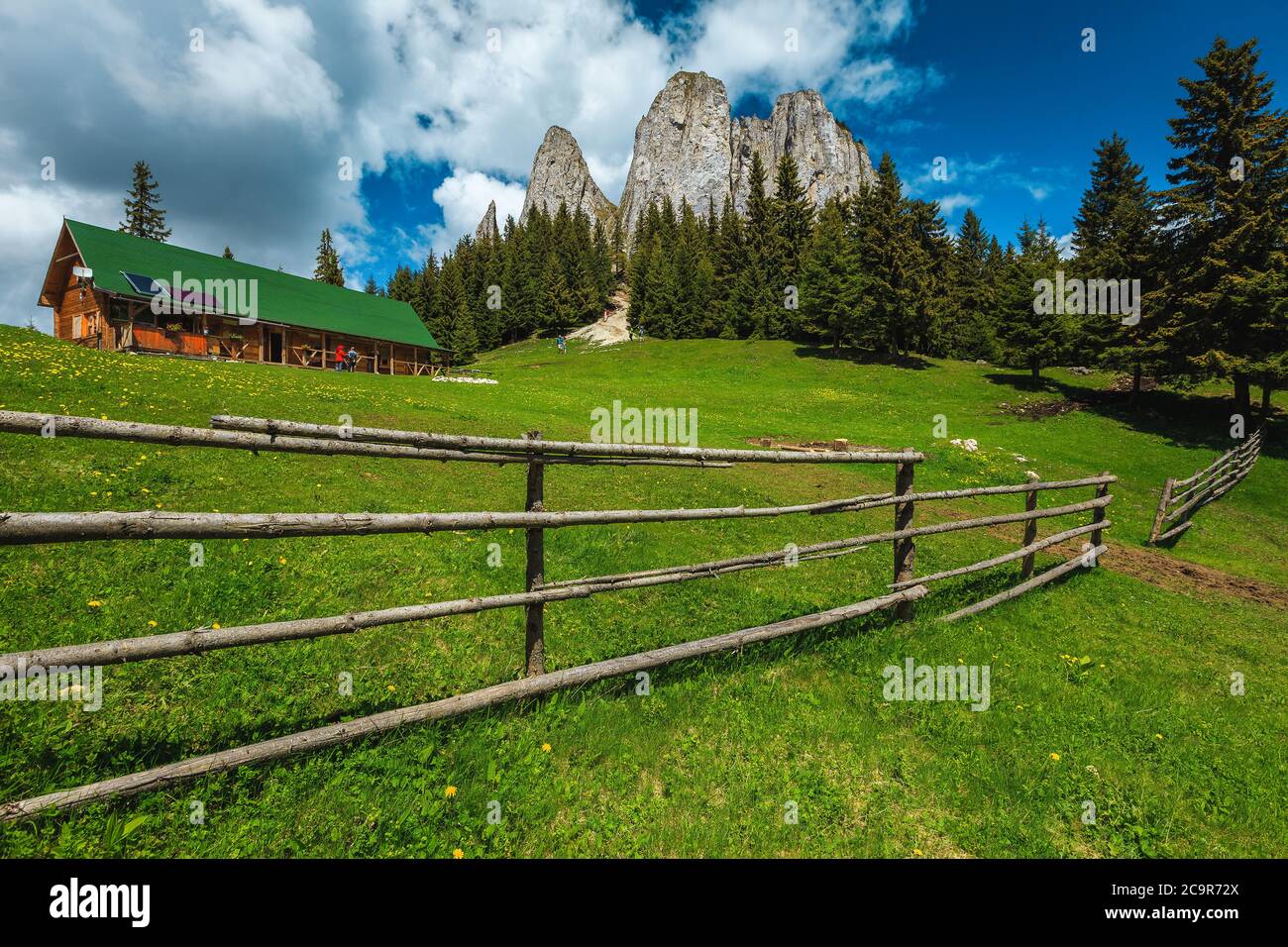 Bella casa di legno vicino alte scogliere nella foresta, Piatra Singuratica, montagne Hasmasul Mare, Carpazi, Romania, Europa Foto Stock