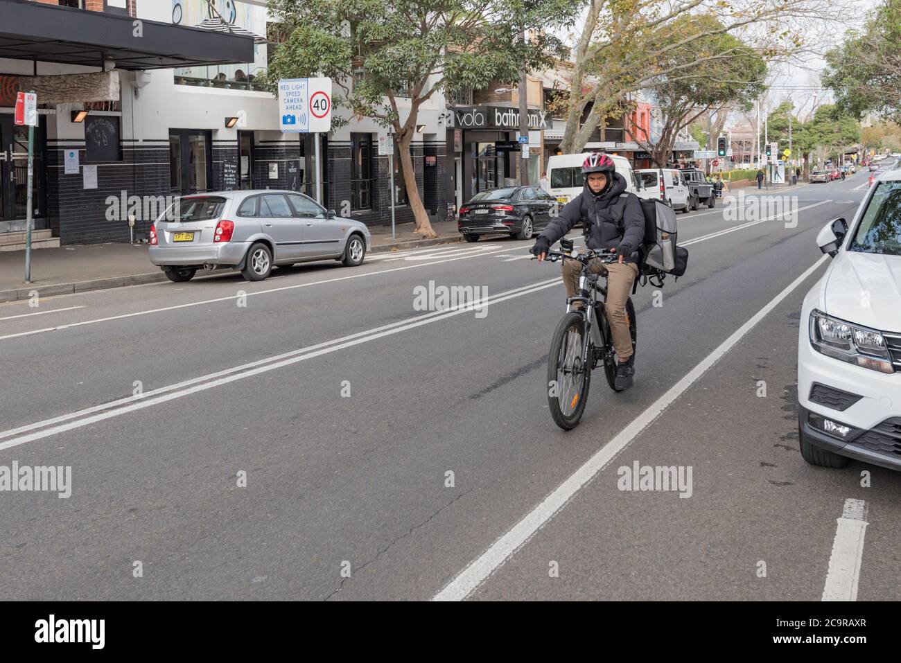 Indossando una balaclava, guanti e una giacca, un corriere di cibo per biciclette (Uber mangia) guida la sua bicicletta su Crown Street a Surry Hills, Sydney, Australia Foto Stock
