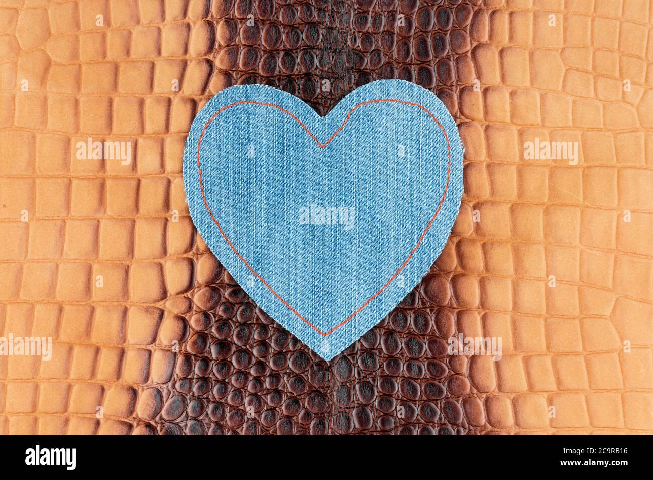 Il cuore in denim blu si trova sulla pelle di coccodrillo marrone. Vista dall'alto Foto Stock