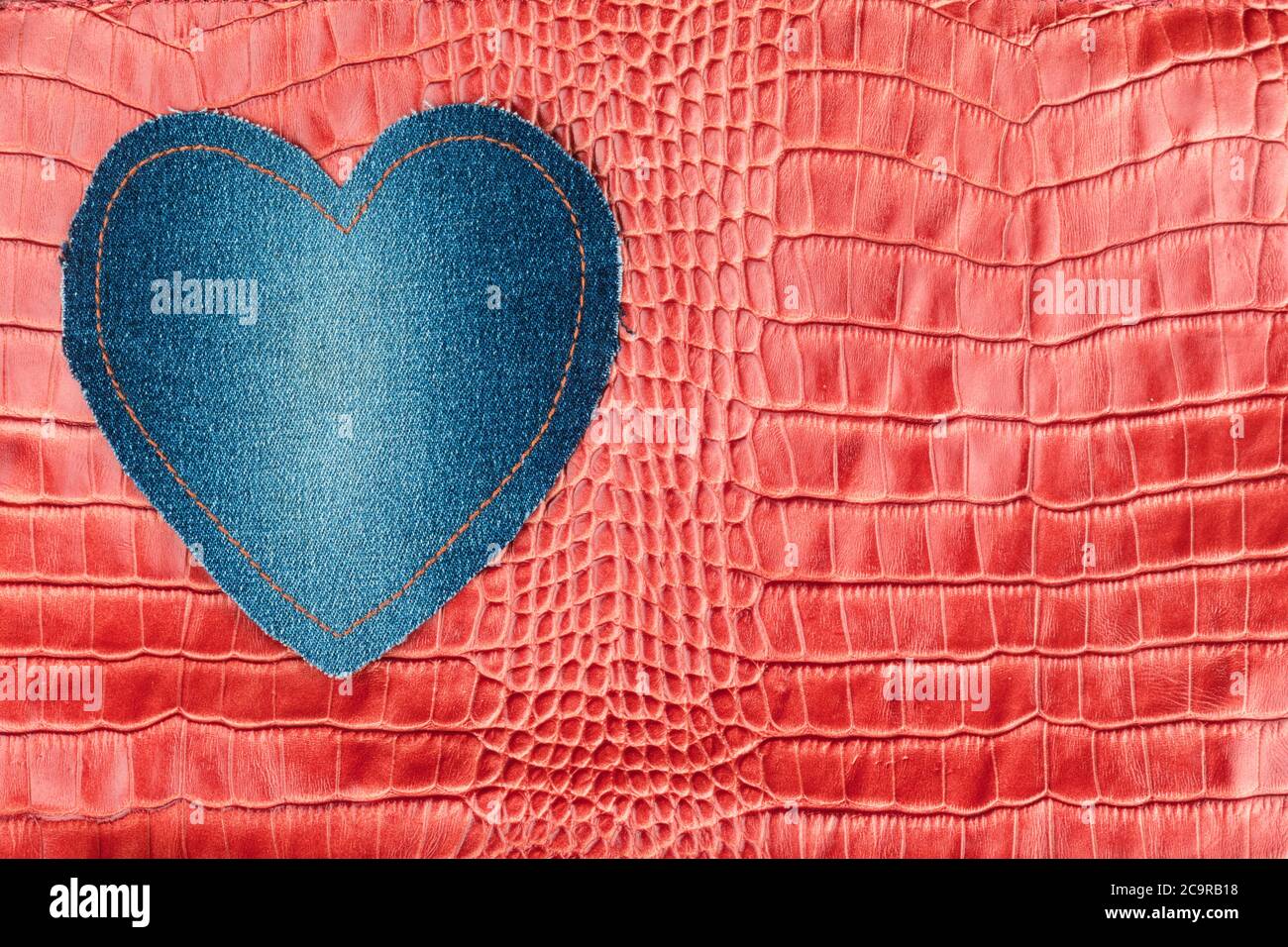 Il cuore in denim blu si trova sulla pelle di coccodrillo rosso. Vista dall'alto Foto Stock