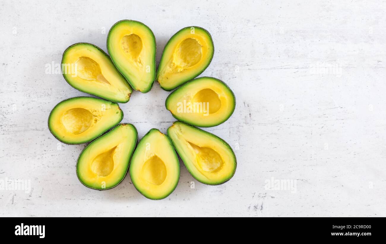 Vista dall'alto in basso, 8 metà avocado disposte in cerchio su lavagna bianca, banner con spazio per il testo a destra Foto Stock