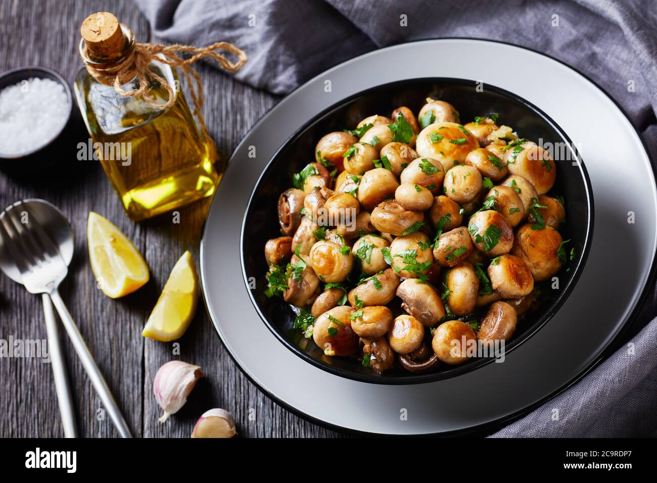 Piatto a basso contenuto calorico e a basso contenuto di grassi tapas spagnole ai funghi all'aglio al ajillo champignons arrostiti all'aglio con prezzemolo, aglio, succo di limone su un piatto nero Foto Stock