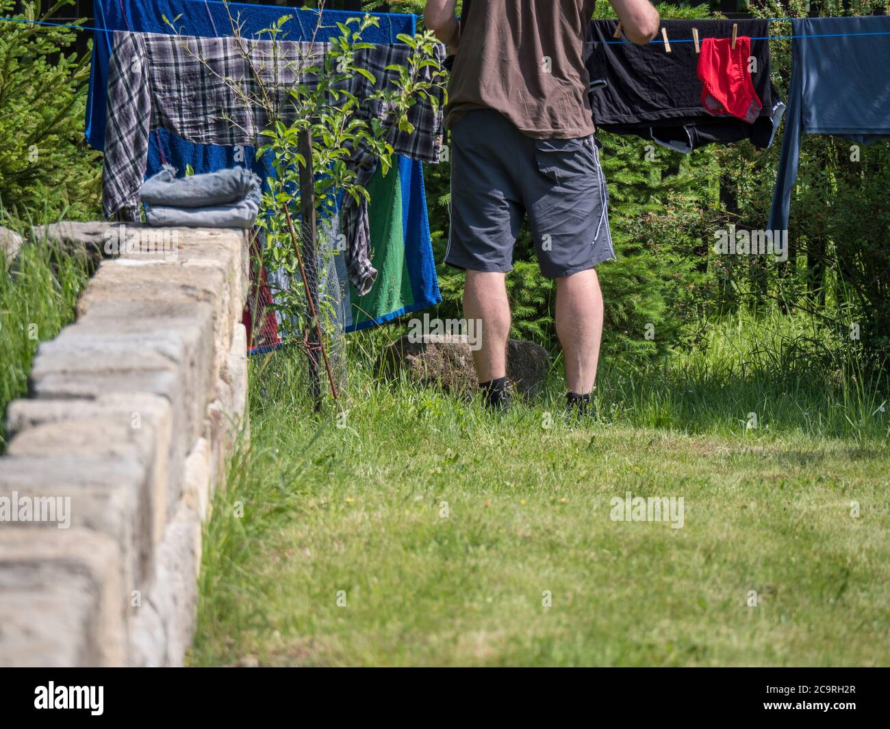 Giovane uomo appeso su lavanderia su una stendibiancheria da giardino, parete in arenaria, spazio per fotocopie Foto Stock