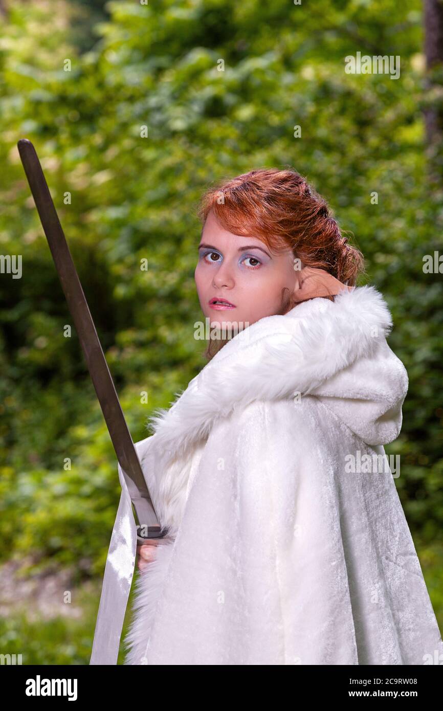 Ritratto di una donna decapitata con orecchie di elfo e mantello bianco che tiene in mano una spada. Foto Stock