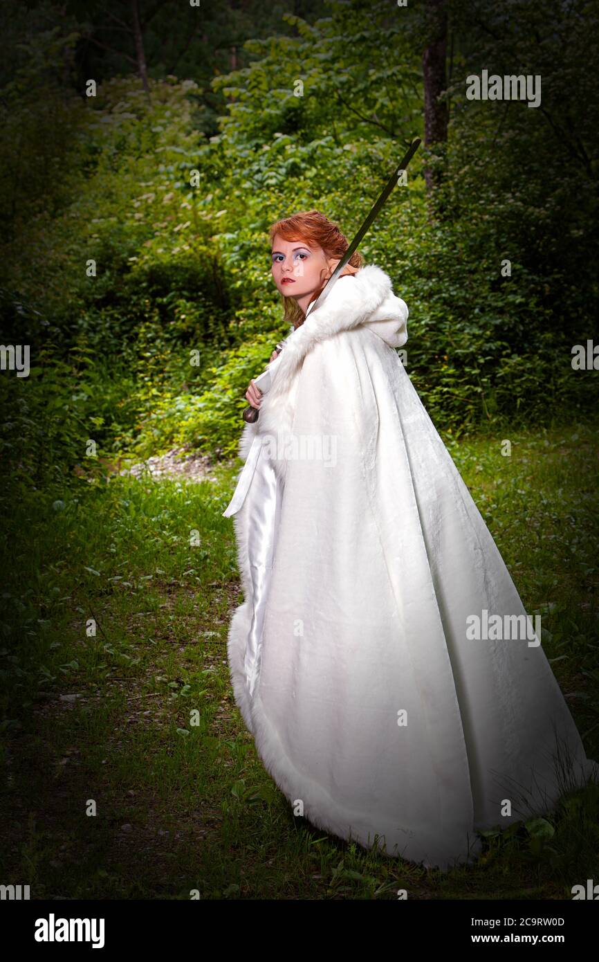 Ritratto di una donna decapitata con orecchie di elfo e mantello bianco che tiene in mano una spada. Foto Stock