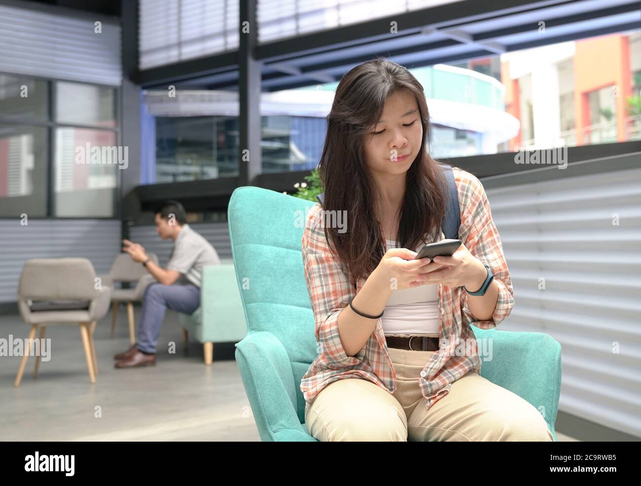 Giovane ragazza cinese con un uomo dietro di lei utilizzando il cellulare per la SMS o la lettura online. Stile di vita digitale. Foto Stock