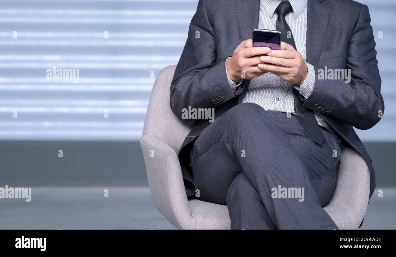Uomo d'affari nel vestito di affari usando il cellulare al testo o al messaggio. Concentratevi sulle mani con il dispositivo. Foto Stock