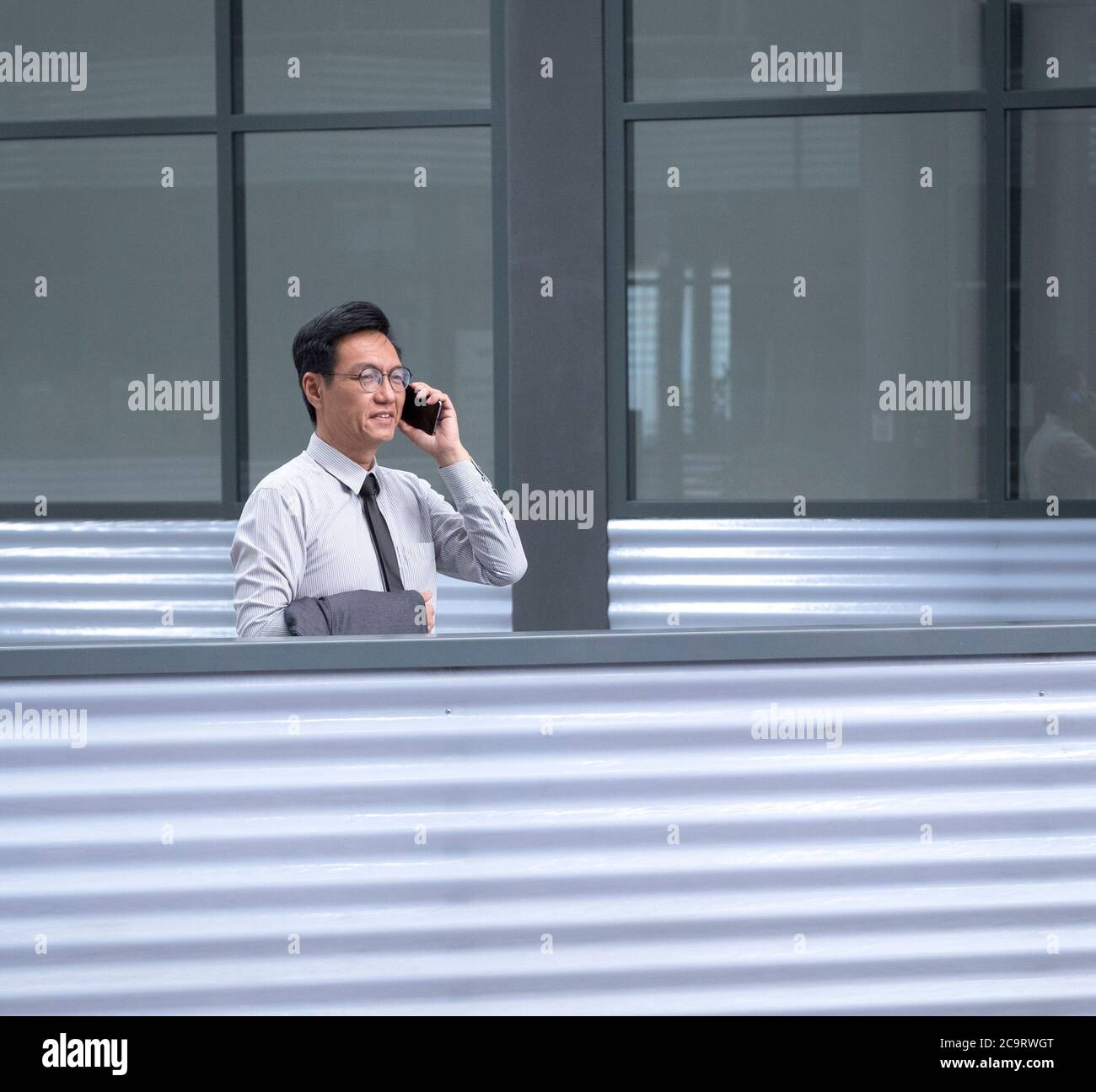 Uomo d'affari cinese in piedi, sorridendo e parlando sul suo cellulare Foto Stock