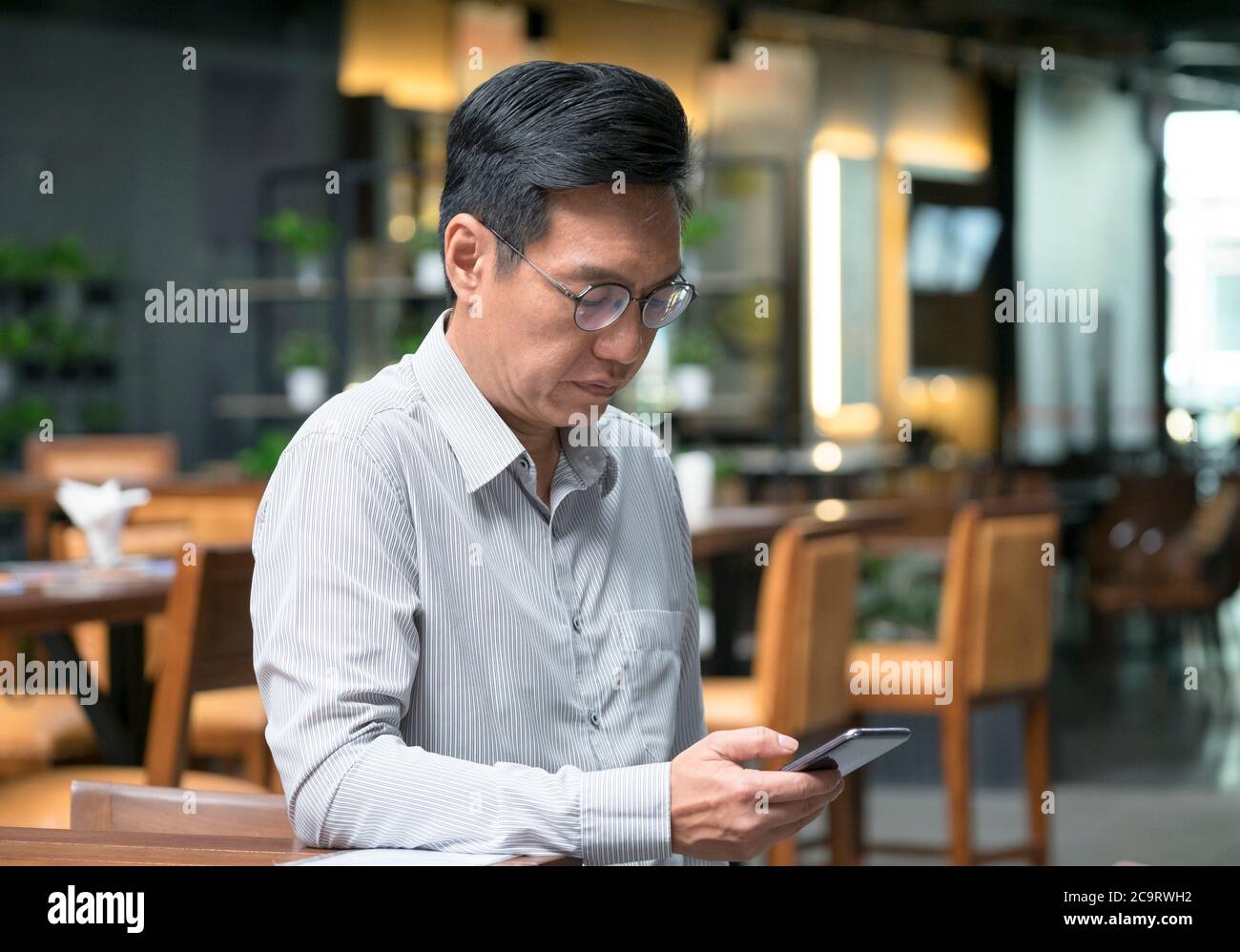 Uomo d'affari cinese che indossa una giacca, sorridendo e guardando il cellulare in mano. Foto Stock