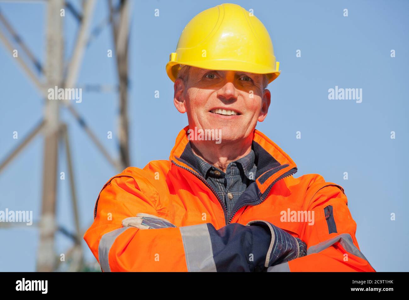 Ritratto di un ingegnere sorridente, un caposquadra o un lavoratore con indumenti protettivi e un elmetto di fronte a sfondo industriale con cielo blu Foto Stock