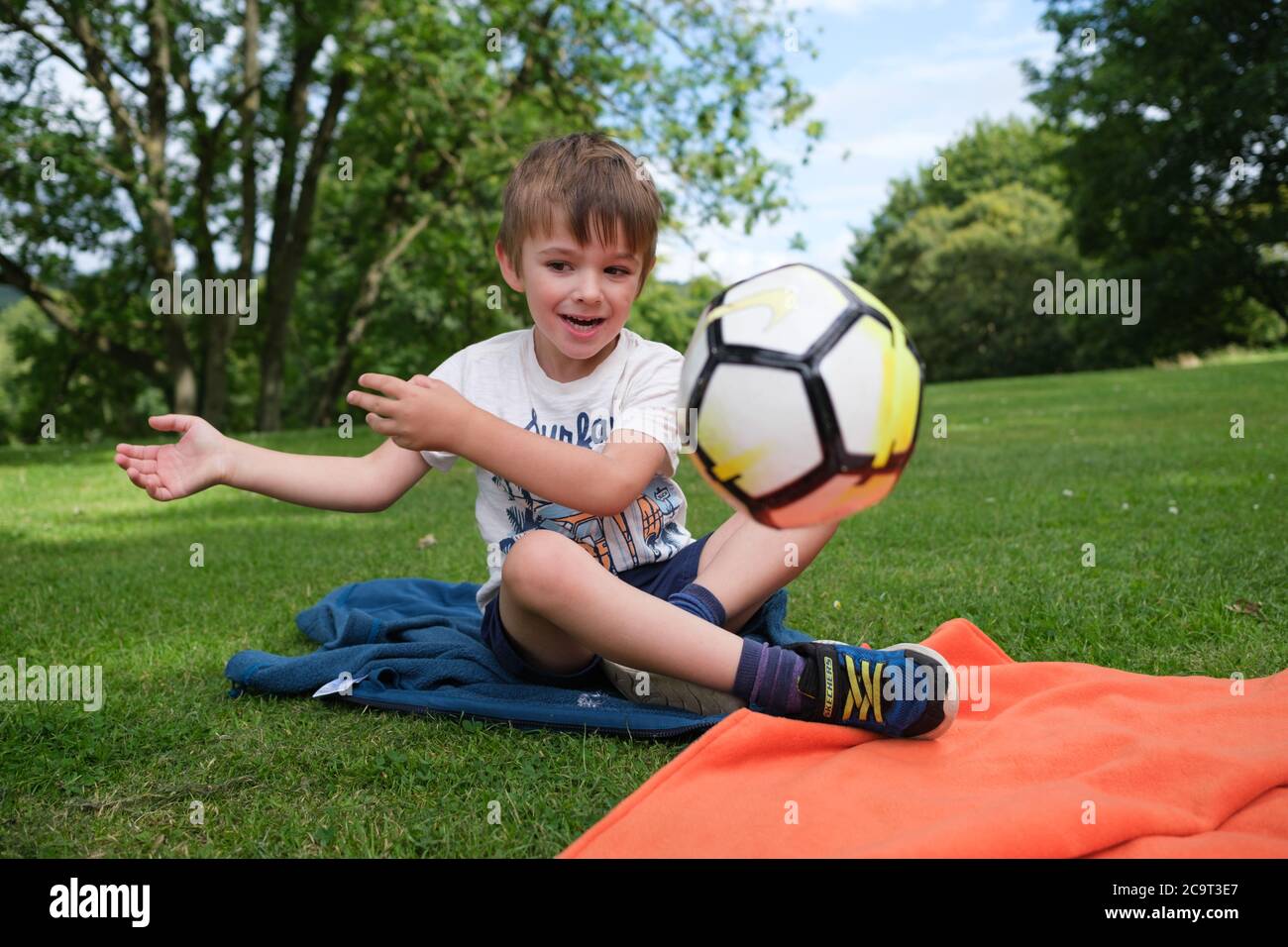 Ragazzo di quattro anni sedette sull'erba gettando una palla Foto Stock