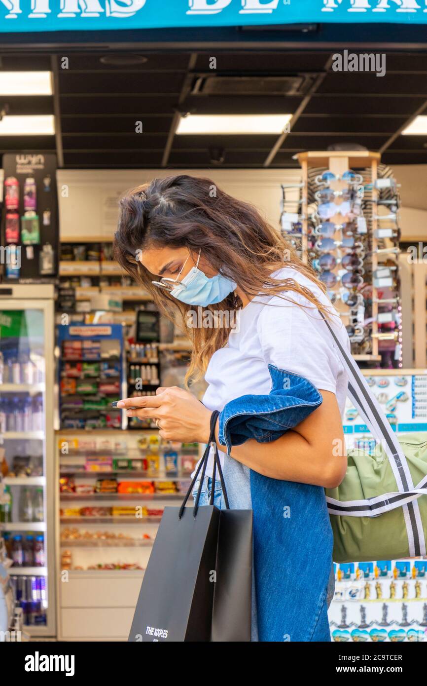 Giovane donna in maschera controlla il telefono cellulare di fronte al negozio a Marsiglia francia Foto Stock