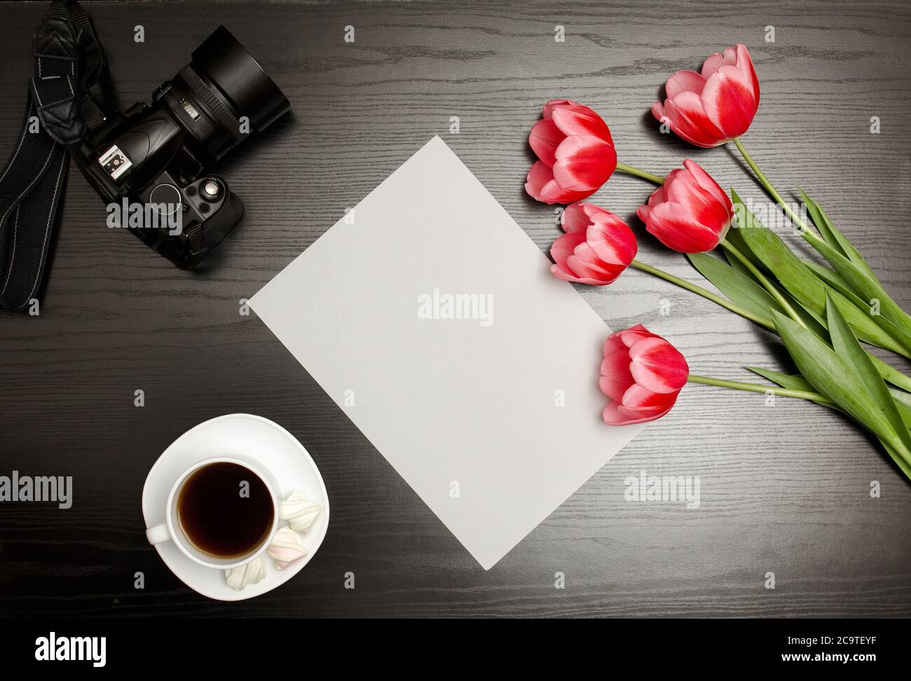 Fogli puliti di carta, tulipani rosa, una macchina fotografica e una tazza di caffè. Tavolo nero. Vista dall'alto Foto Stock