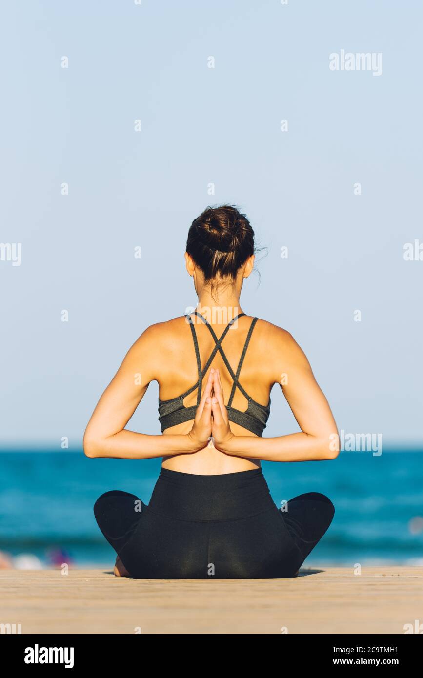 giovane donna dalla parte posteriore che fa yoga di fronte al mare in una giornata soleggiata all'aperto Foto Stock