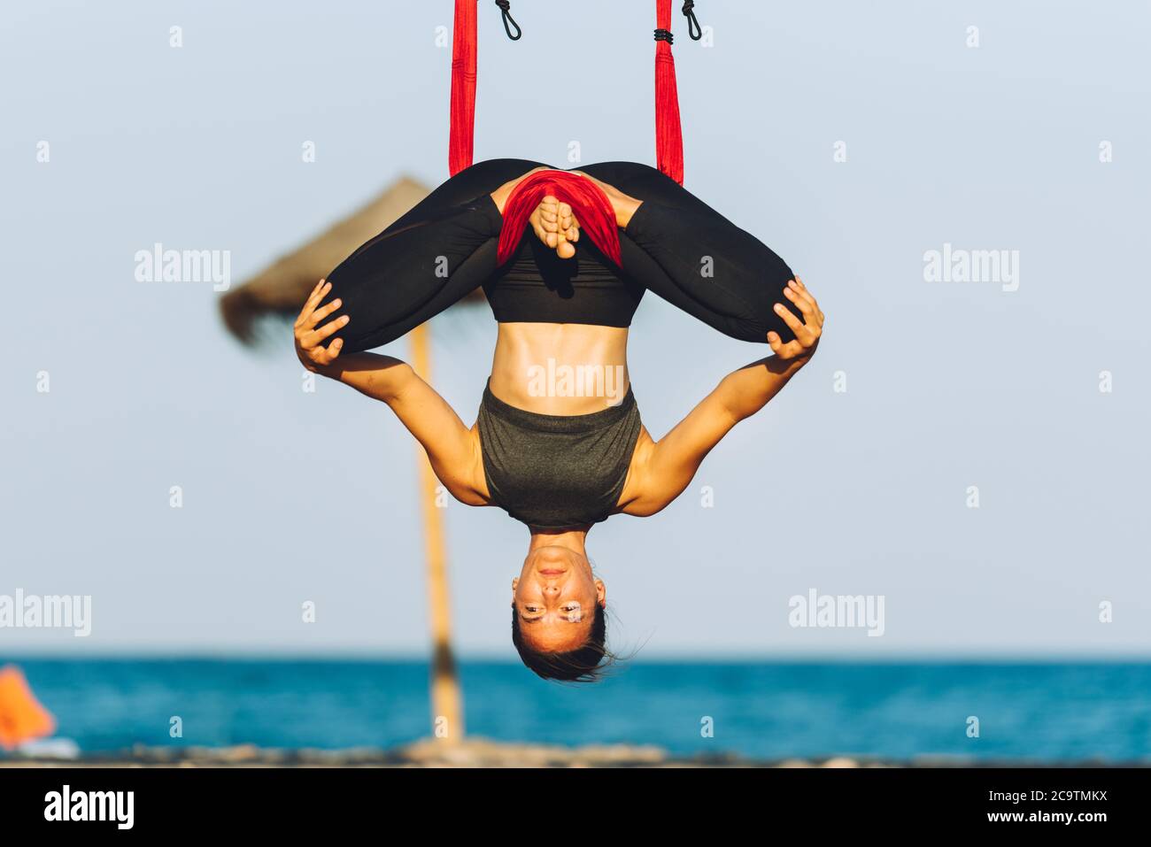 giovane donna che fa esercizi di yoga con swing capovolto sulla spiaggia di fronte al mare in una giornata di sole Foto Stock