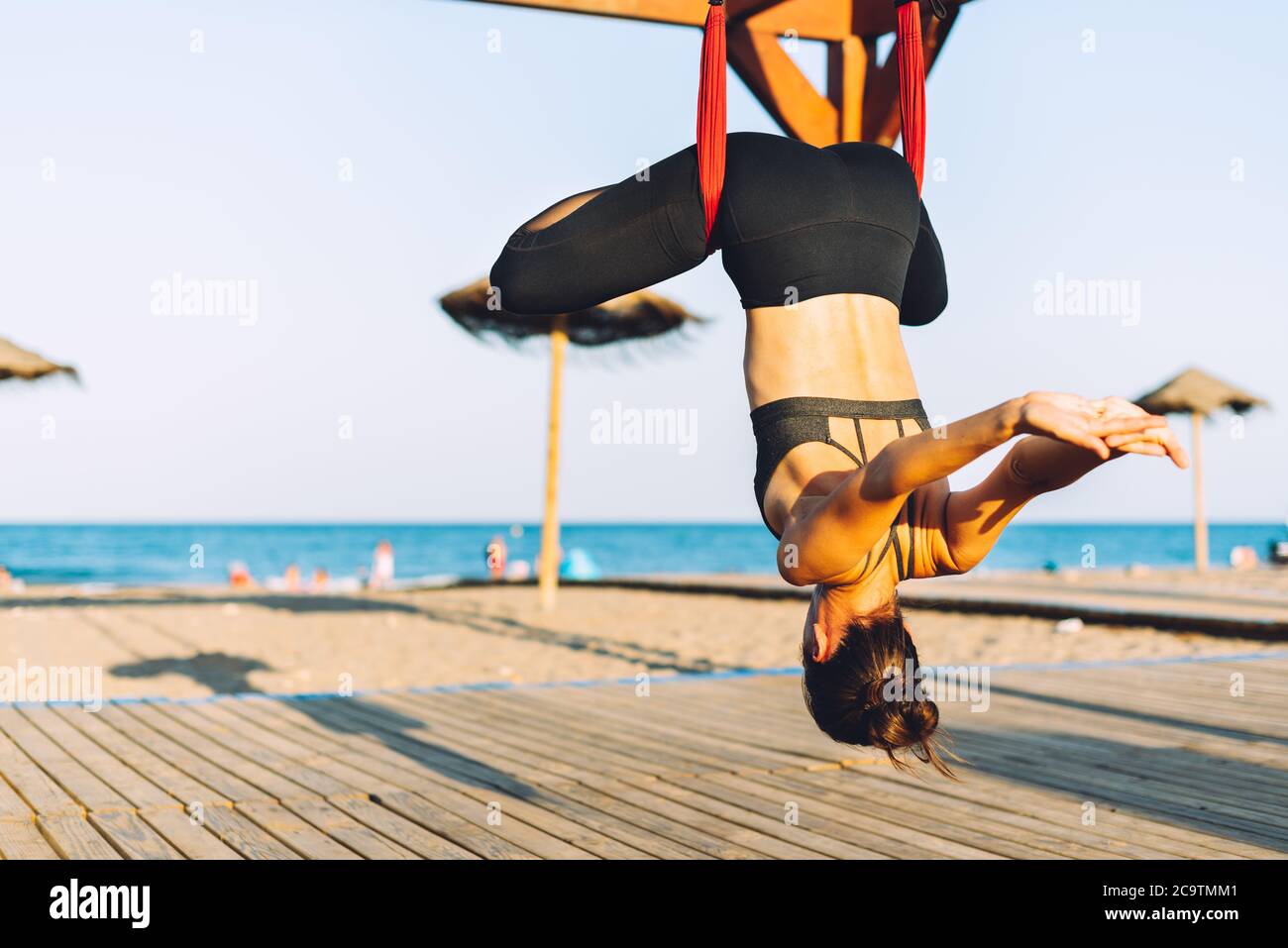 giovane donna che fa esercizi di yoga con swing capovolto sulla spiaggia di fronte al mare in una giornata di sole Foto Stock
