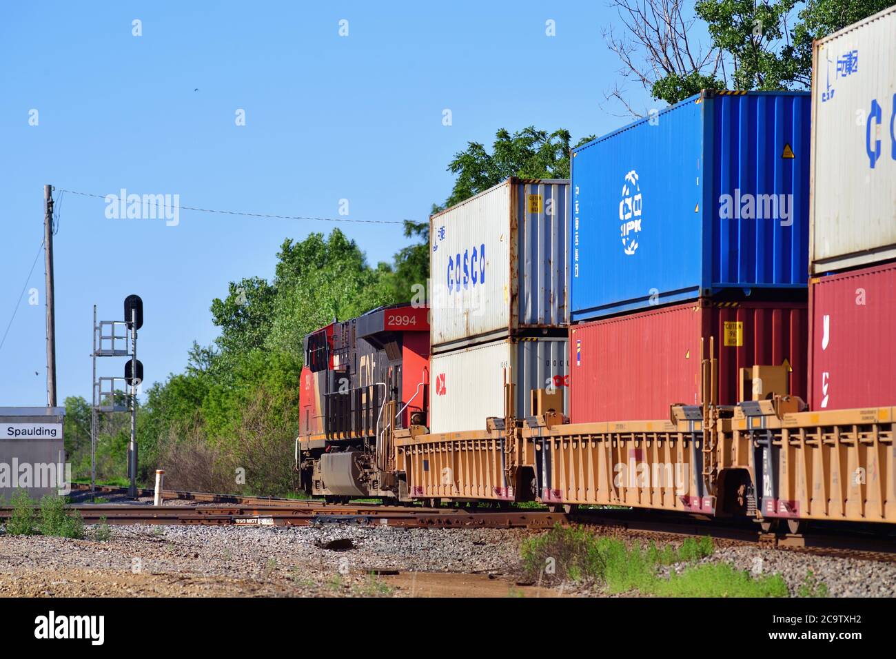Bartlett, Illinois, Stati Uniti. Un'unica locomotiva ferroviaria nazionale canadese posta alla fine di un treno merci intermodale spinge attraverso un incrocio. Foto Stock