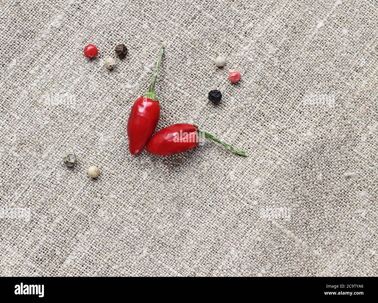 Capsicum rosso caldo (peperoni) a forma di cuore e pochi pezzi di pepe misto su fondo tessile grigio. Foto Stock