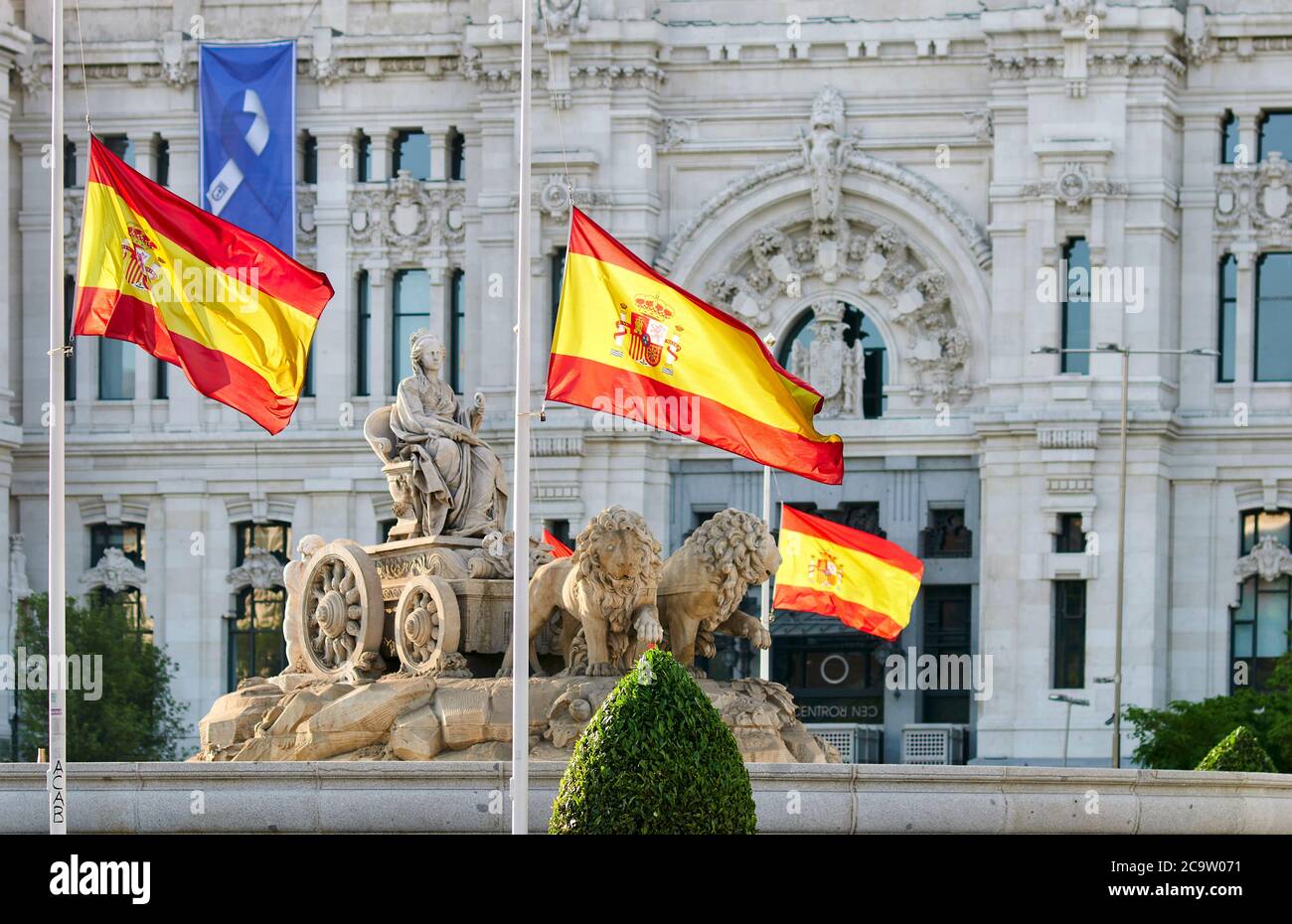 Madrid, Spagna - 25 maggio 2020: Le bandiere spagnole volano a metà albero come segno di lutto per coloro che sono stati uccisi da Covid-19 nella Plaza de Cibeles a Madrid Foto Stock