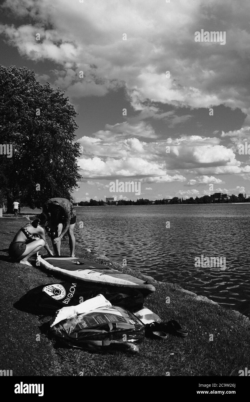Bianco e nero - due persone che gonfiano un SUP sul lato del lago Dow's in una bella giornata estiva, Ottawa, Ontario, Canada. Foto Stock