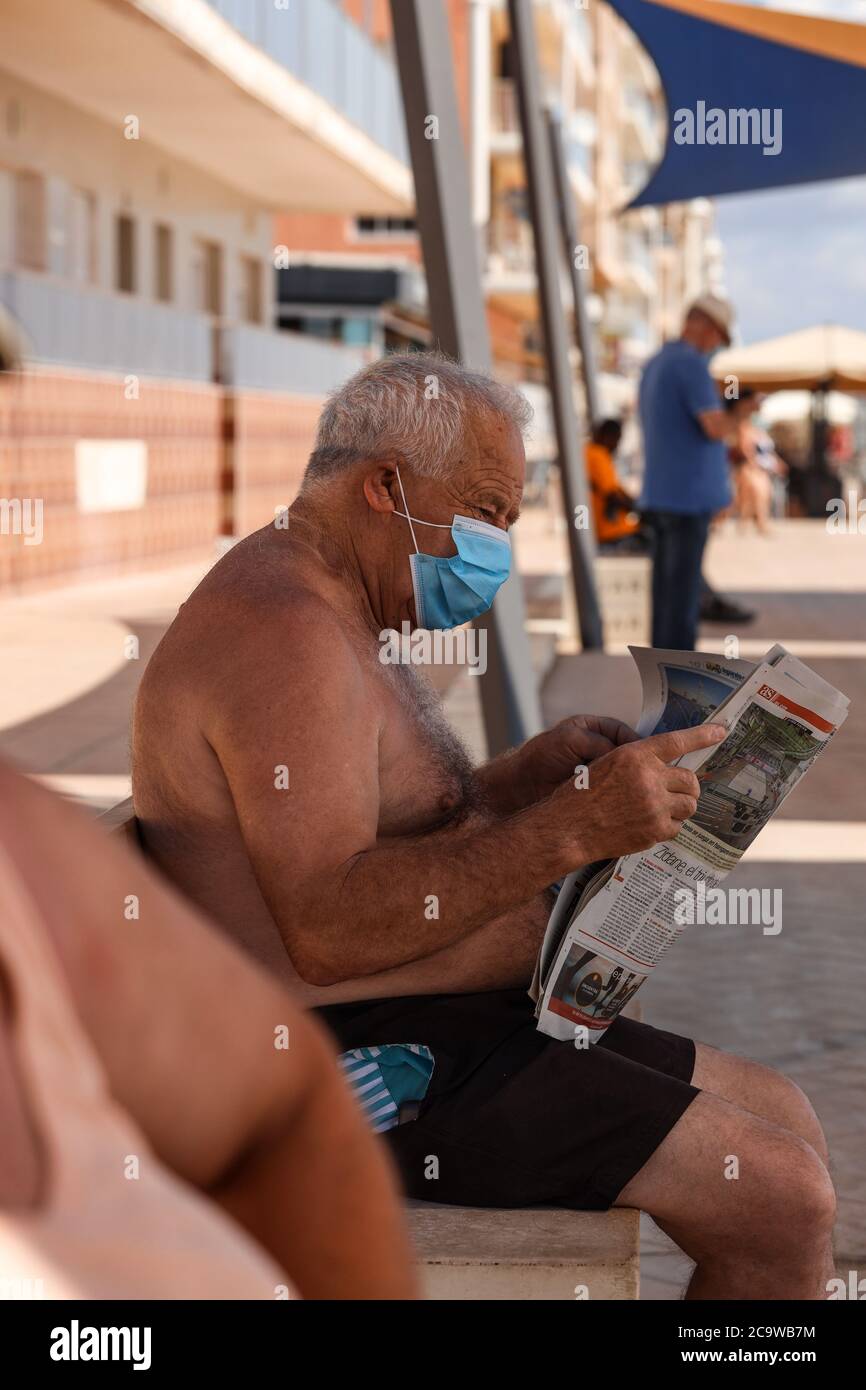 Un uomo anziano sedette a leggere un giornale mentre indossava una maschera durante il 2020 Coronavirus Pandemic, Guardamar, Spagna Foto Stock