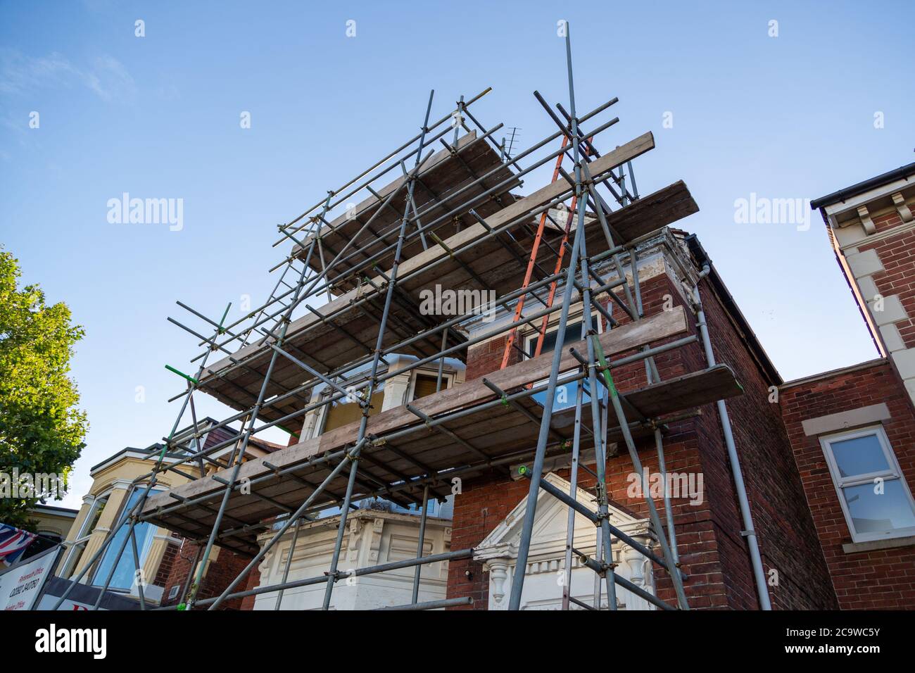 un edificio in mattoni circondato da pali per ponteggi pronti per lavori di costruzione Foto Stock