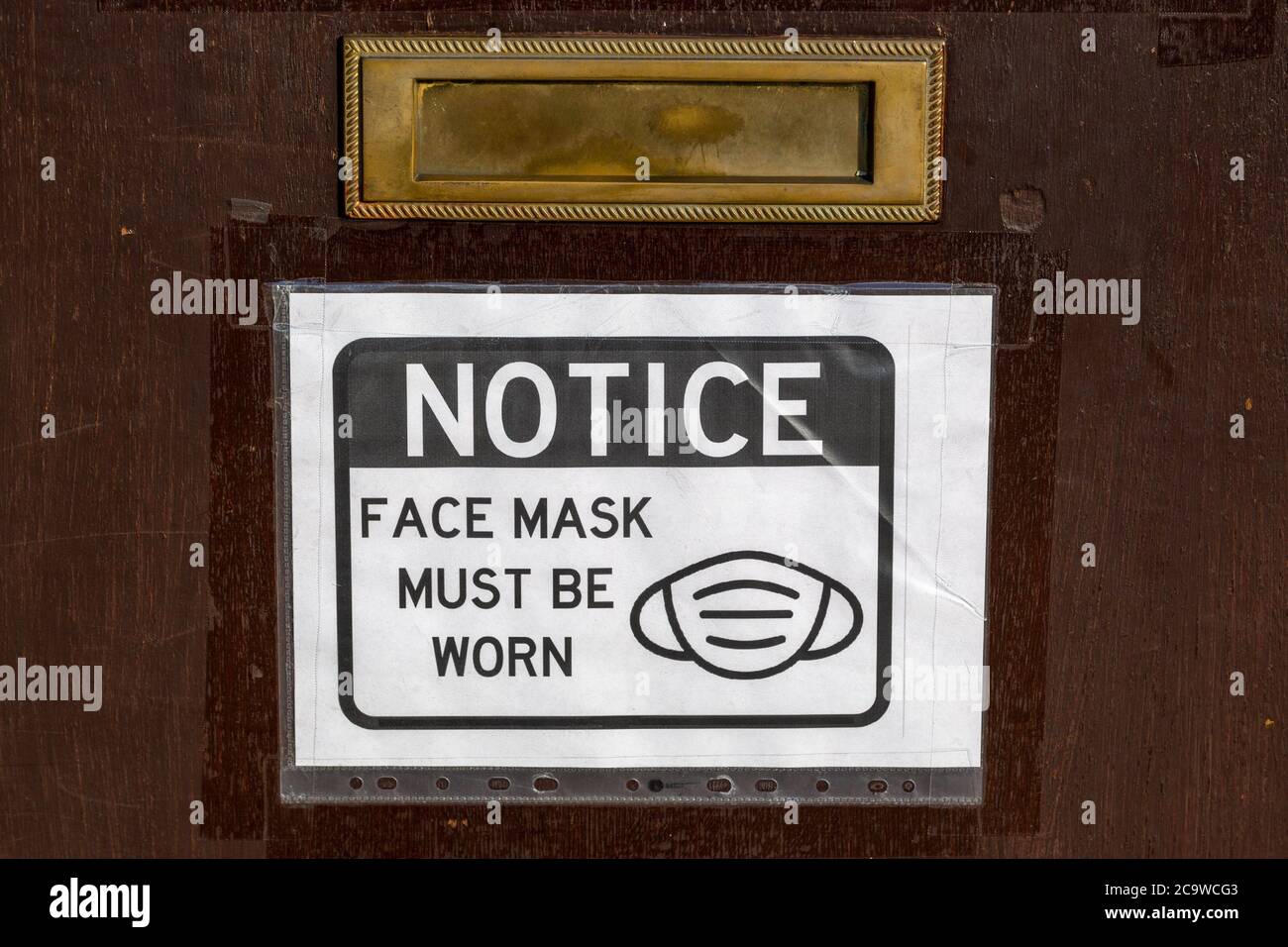 un avviso su una porta anteriore di un'azienda che dichiara le maschere facciali devono essere avvisate in conformità con il governo Linee guida durante il Covid-19 Foto Stock