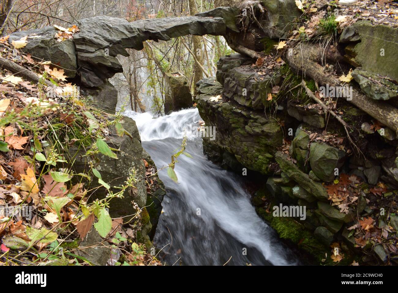 Una lunga esposizione di acqua in rapido movimento che scorre sotto un arco di pietra naturale su una scogliera Foto Stock