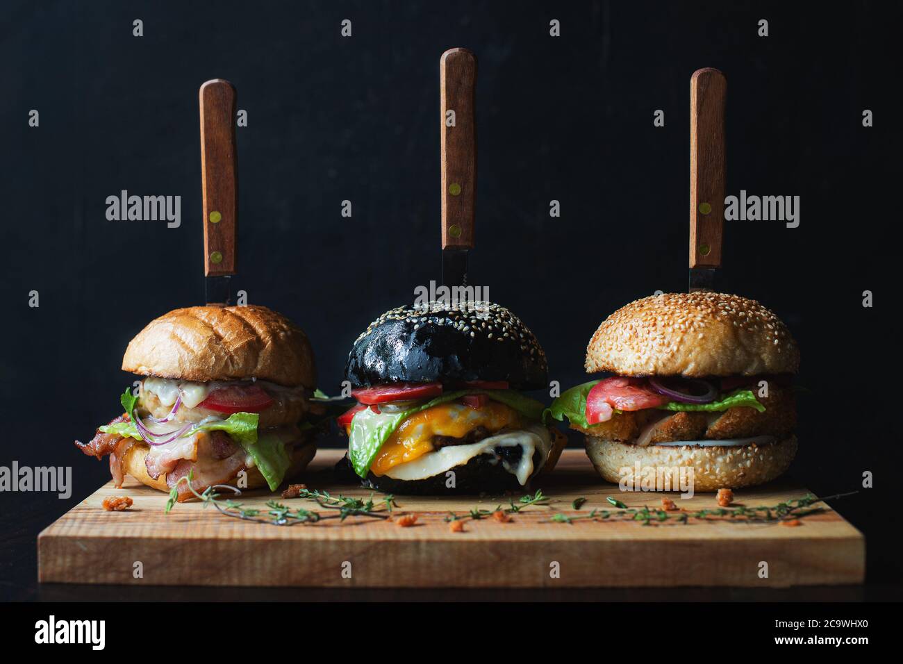 tree deliziosi hamburger fatti a mano con hamburger di carne di manzo e verdure fresche servite con coltelli su tavola di legno. su sfondo scuro. Cibo gustoso. Foto Stock