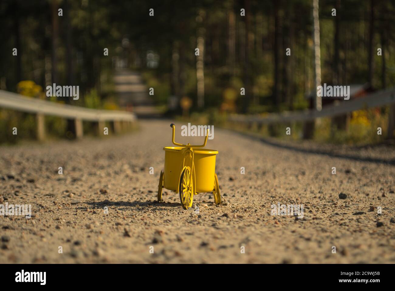 Un triciclo giocattolo giallo su una strada in ghiaia Foto Stock