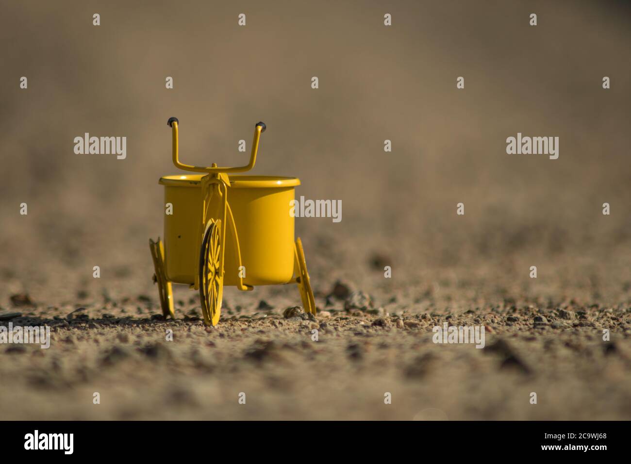 Un triciclo giocattolo giallo su una strada in ghiaia Foto Stock